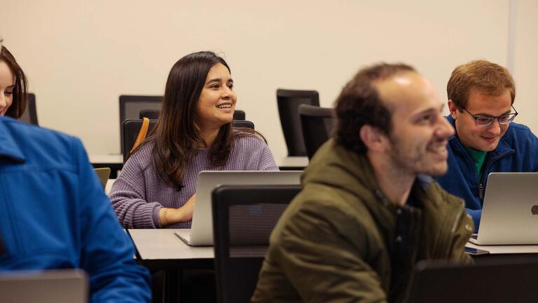 Students in class smiling and sitting in front of laptops