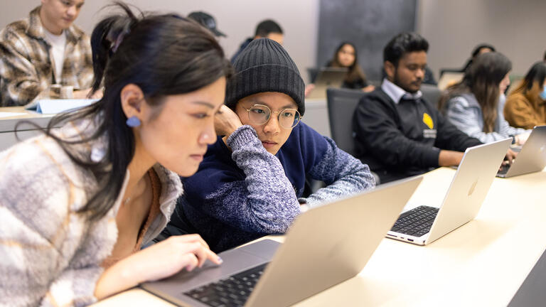 Two students in class look at a laptop