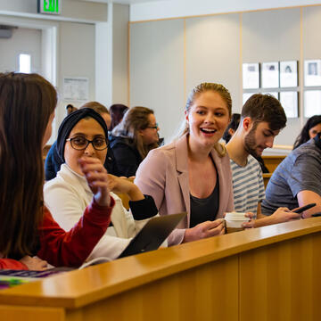 A number of students talk while seated in a jury box.