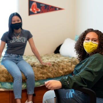 Two students talk while sitting in a dorm room.
