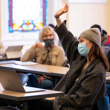 Student sitting at a table raises hand in class