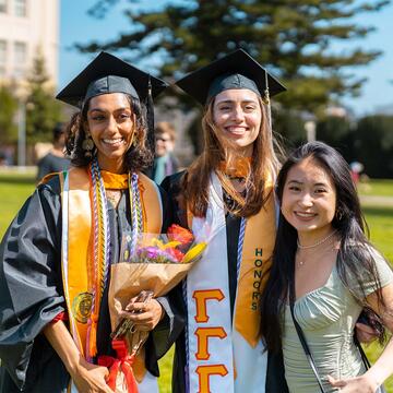 Three alumni dressed in their graduation gowns.