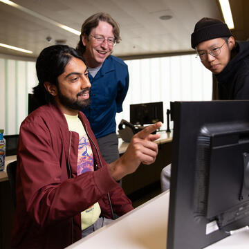 Students and professor look at a computer monitor together