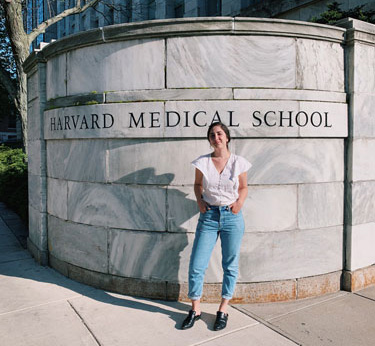 Kayla standing in front of a sign that reads "Harvard Medical School"