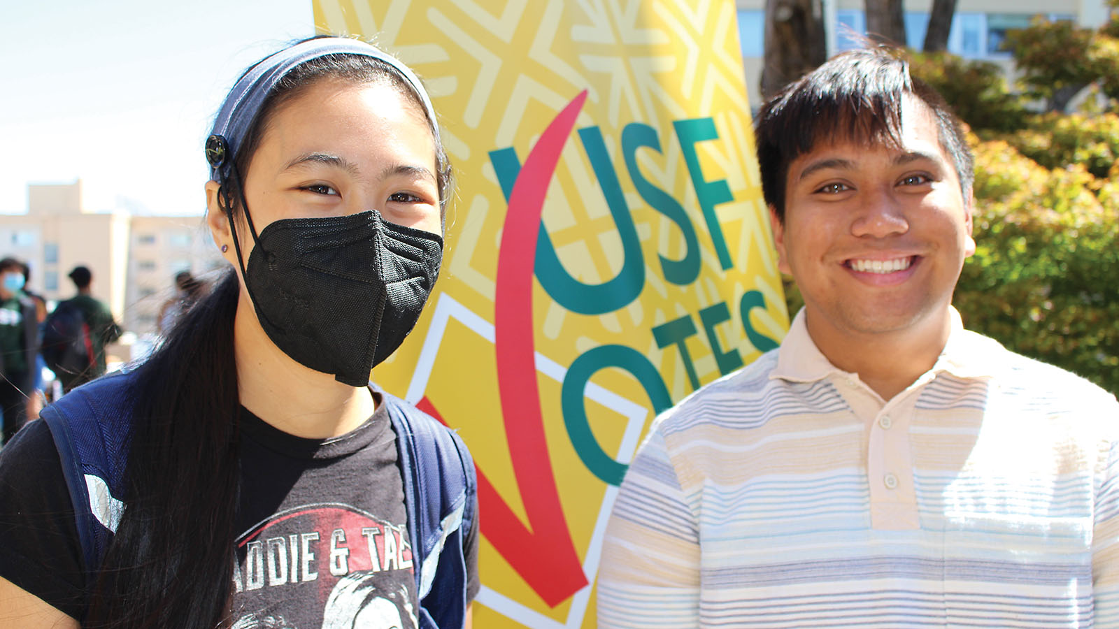 Two students stand in front of a USF Votes banner