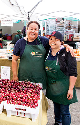 Two grocers pose with arms around each other at a stand.