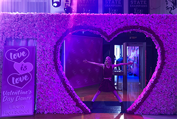 Ellora Coombs ’12 on the set of 13 Reasons Why standing in the gymnasium in a heart hsaped box
