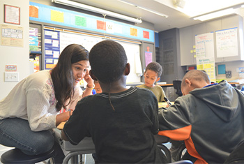 Person kneeling down with children in a classroom