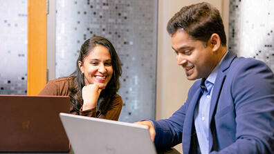 Two USF students working on their laptops and chatting