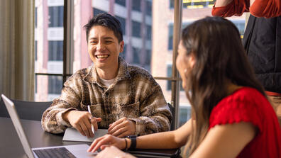 students smile while using laptop together
