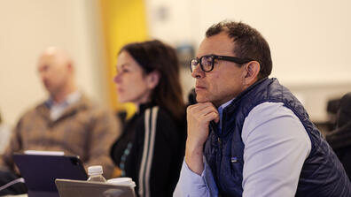 Adult wearing glasses and vest focused in class