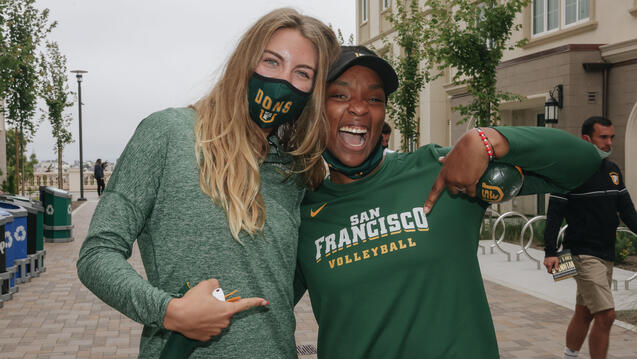 Two athletes hug and point to a shirt with a USF logo on it.