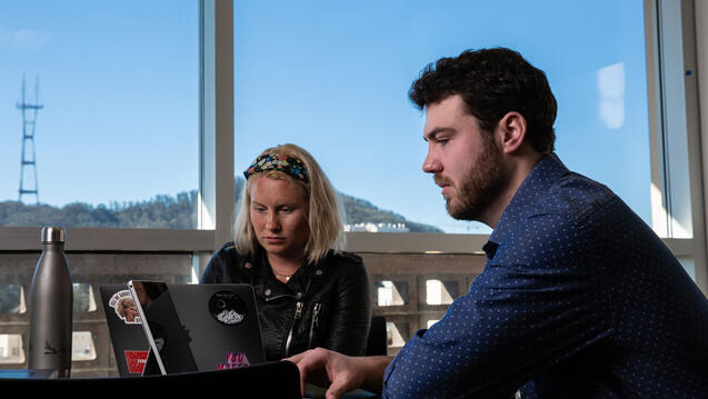 Two students study in front of a window at the library.