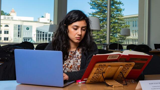 Student studies with a book and a laptop in the library.