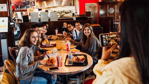 A student takes a photo of a group of students eating at a restaurant.