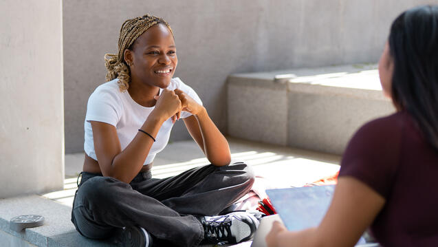 Two students talk while sitting on a wall at Lo Schiavo Science.