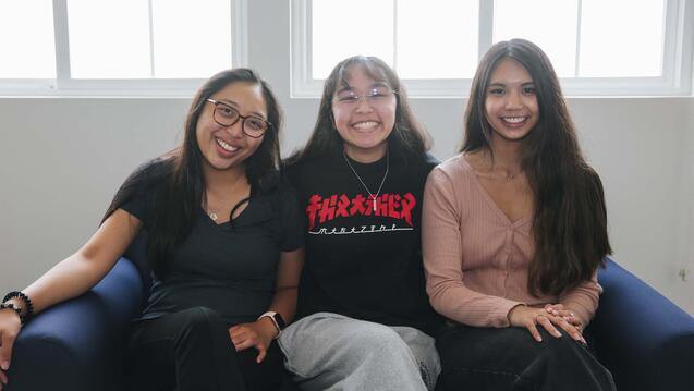 Three students sit together on a couch in the dorms.