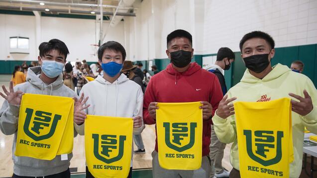 Group of students hold towels with USF on them at Koret Night during orientation.