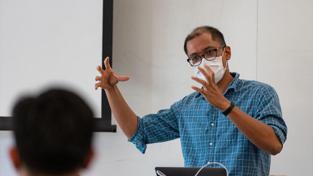 Professor gesturing with both hands lectures at a podium