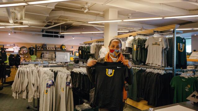 USF provost stands in book store holding USF t-shirt in hand