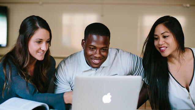 Three students study around a laptop.