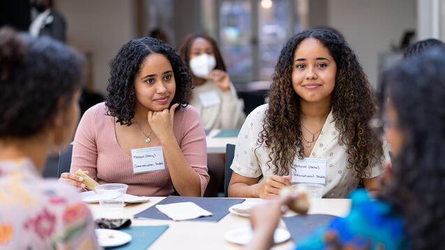 Students chat around a table while eating.