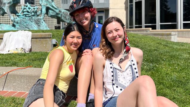 Three students pose for a photo on the lawn.