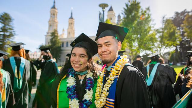 graduates pose outside of St.Ignatius church in their caps and gowns 