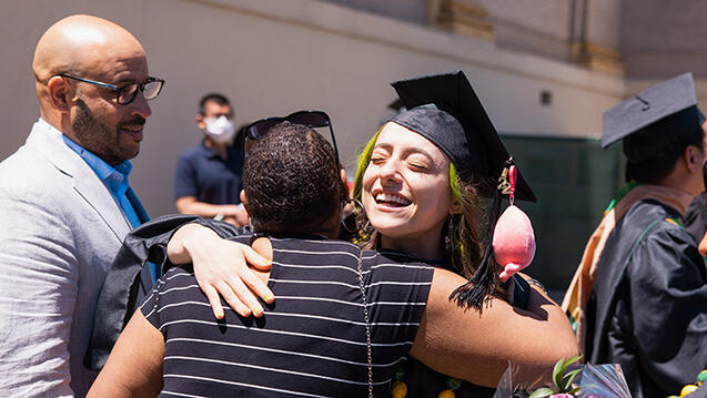 student in graduation gown hugging parent