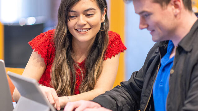 Two students study over a laptop.