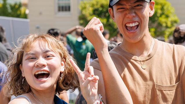 Two students holding their hands up and smiling