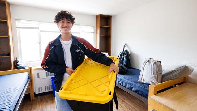 Student holding a storage bin in a dorm room