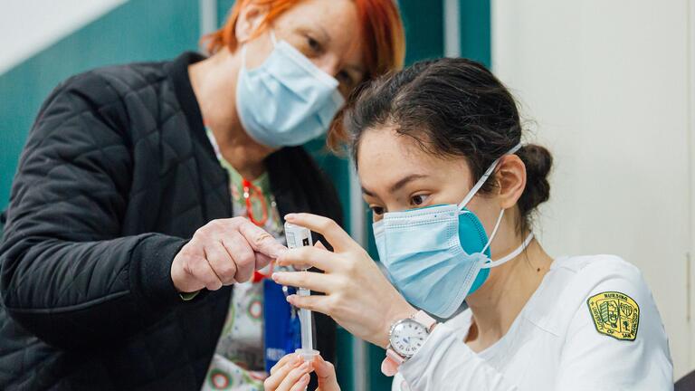 Registered nurse supervises nursing student filling syringe from vial