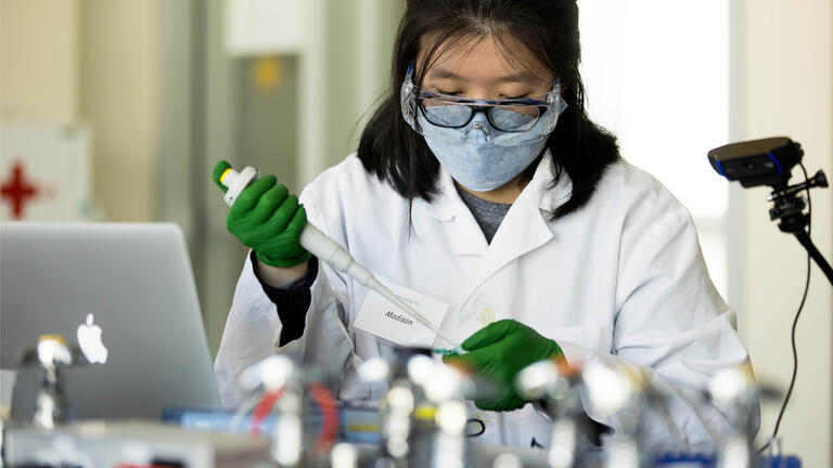 Lab associate in protective gear uses syringe