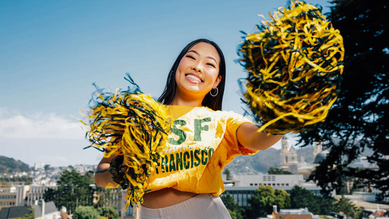 A student wears a USF t-shirt and cheers holding pom-poms