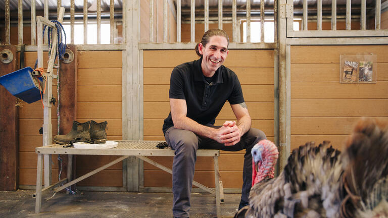 Student sits in a barn near a turkey