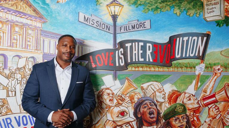 Director stands in front of a mural that reads "Love is the Revolution"