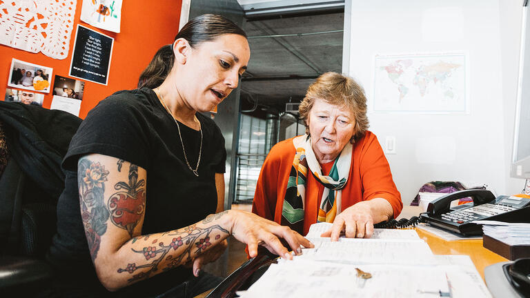 Martha works with a colleague at a desk.