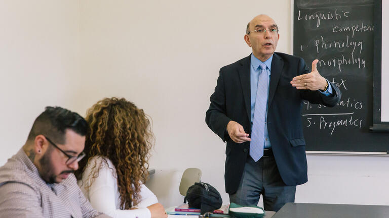 Teacher lectures from the front of a classroom.