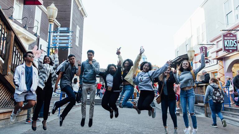 A group of students join hands and jump in the air at Pier 39