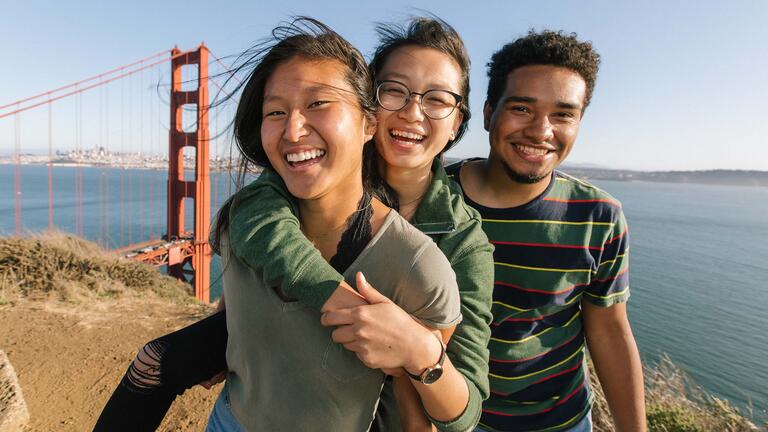 Students hug and laugh on a hill overlook for the Golden Gate Bridge.