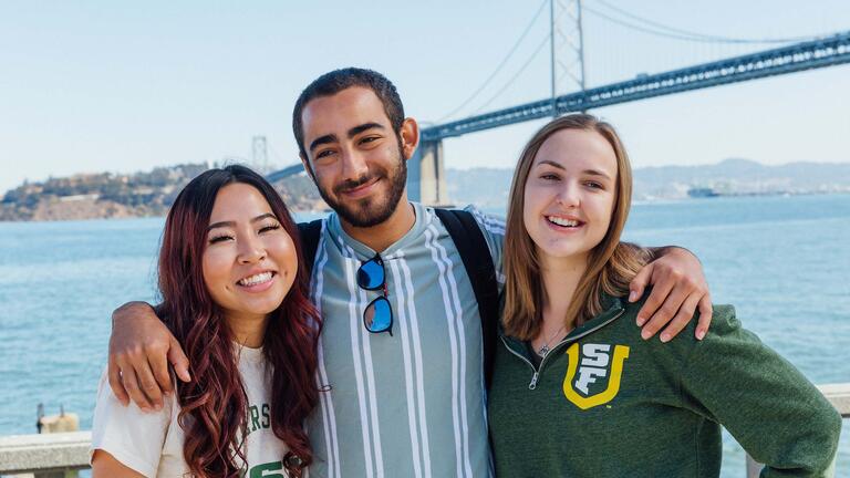 Three students pose in front of the Bay Bridge.