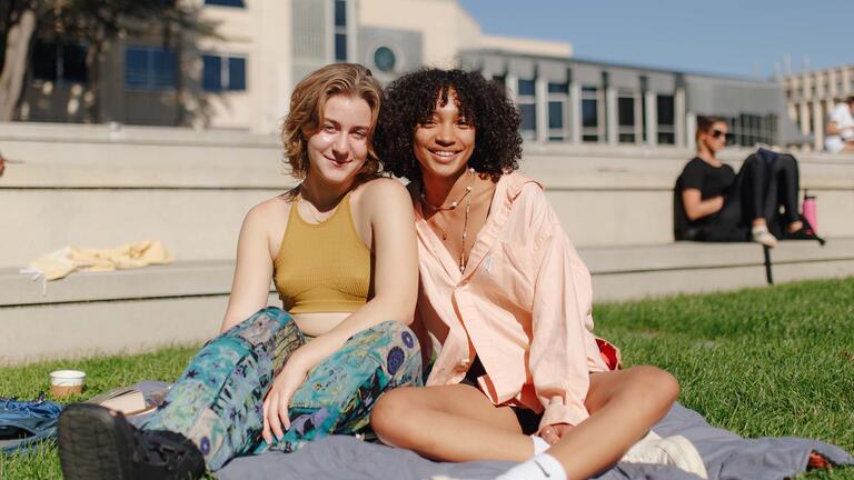 Two students sit on the grass on a sunny day.