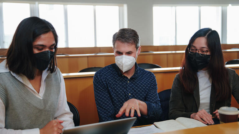 Three students look at study materials together in class.