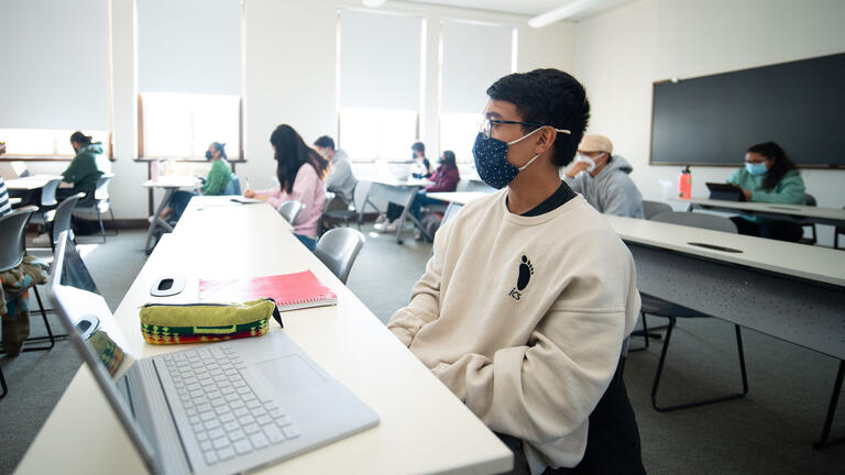 Student with a laptop listens in class