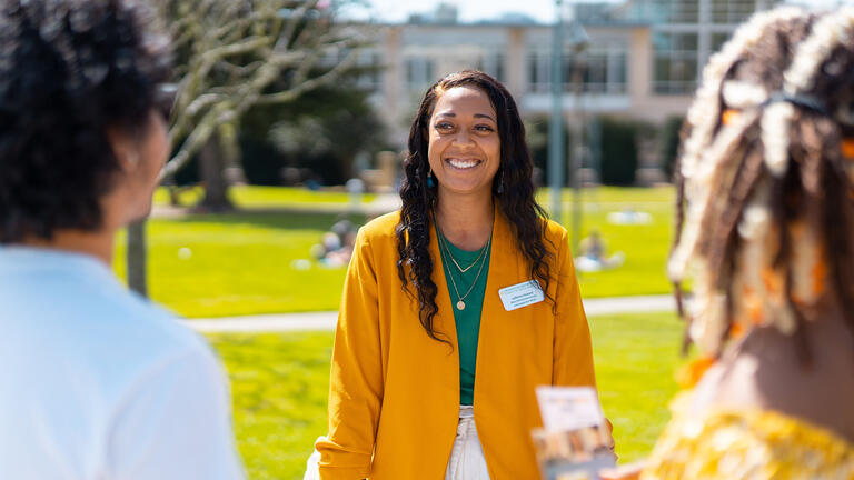 Staff member talks to two students on the lawn.