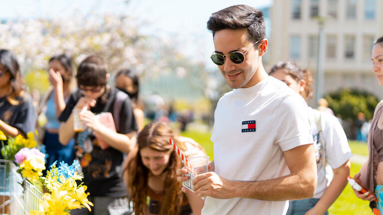 Students examine information on tables at an event on the lawn.