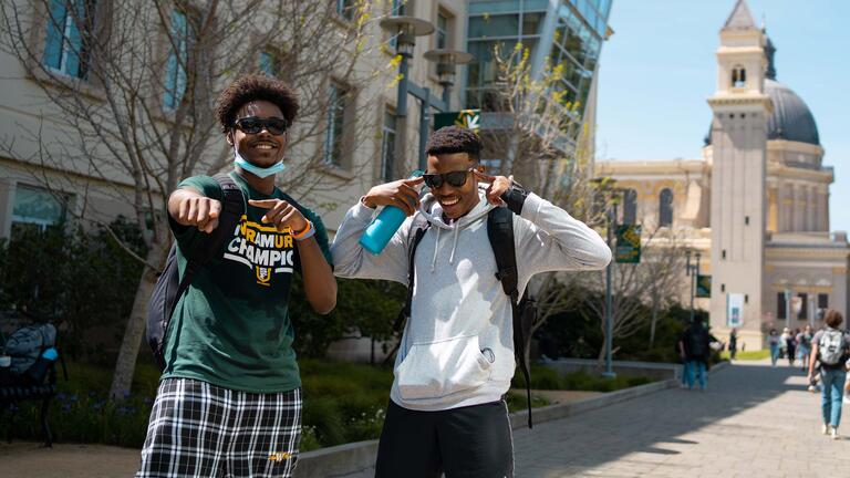 Two students laugh and point at the camera on USF campus.