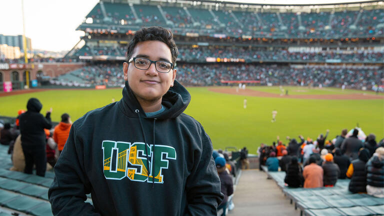 Student in a USF sweatshirt stands at the SF Giants baseball stadium.