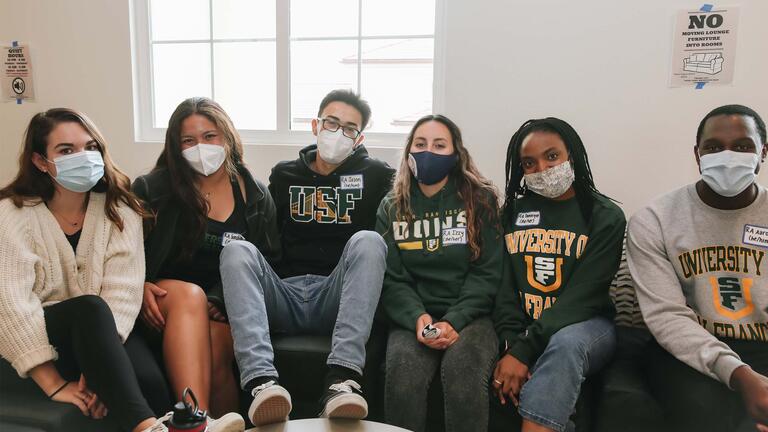 Group of students sit on a couch in the dorms.